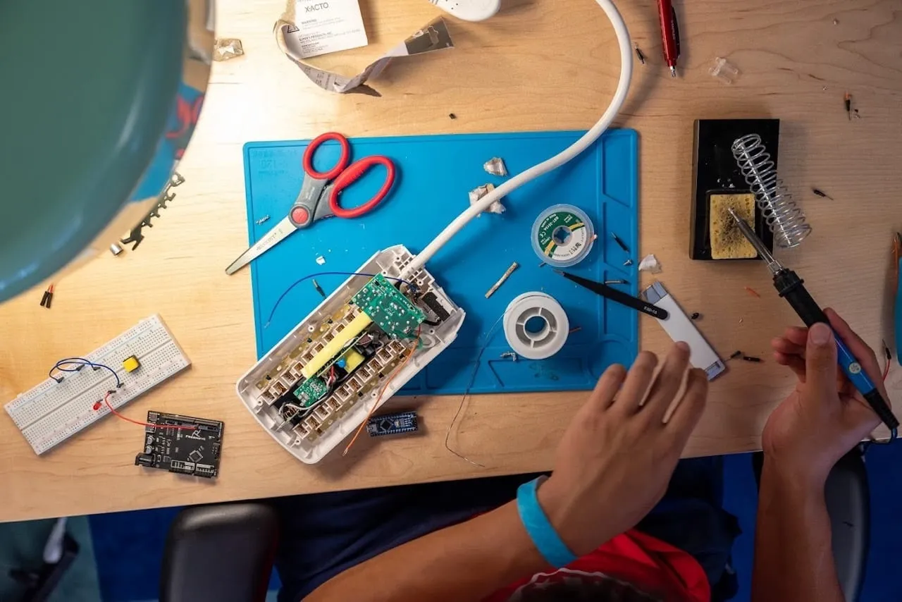 A teenager at a hackathon, soldering an electronics project on a desk.